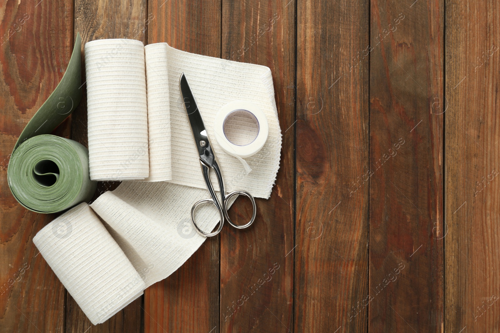 Photo of Medical bandage rolls, sticking plaster and scissors on wooden background, flat lay. Space for text