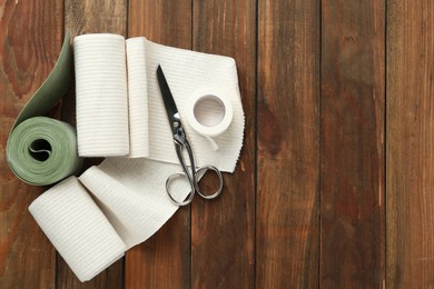 Photo of Medical bandage rolls, sticking plaster and scissors on wooden background, flat lay. Space for text