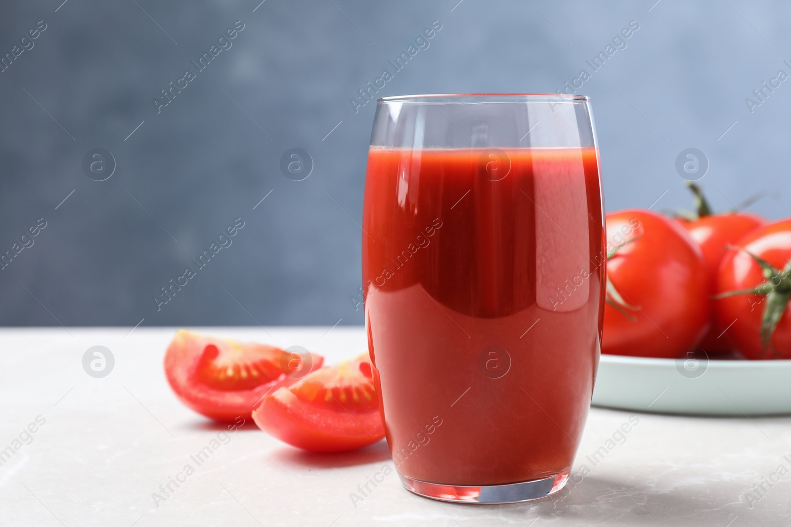 Photo of Delicious fresh tomato juice on light grey marble table table, closeup. Space for text