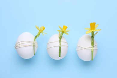 Easter eggs decorated with flowers on light blue background, flat lay