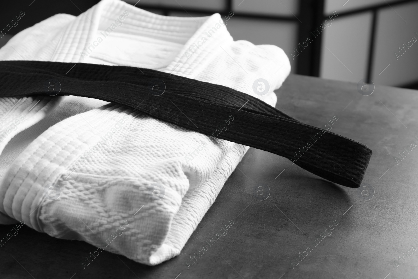 Photo of Martial arts uniform with black belt on grey stone table indoors