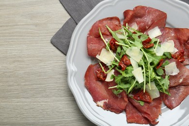 Plate of tasty bresaola salad with sun-dried tomatoes and parmesan cheese on wooden table, top view. Space for text