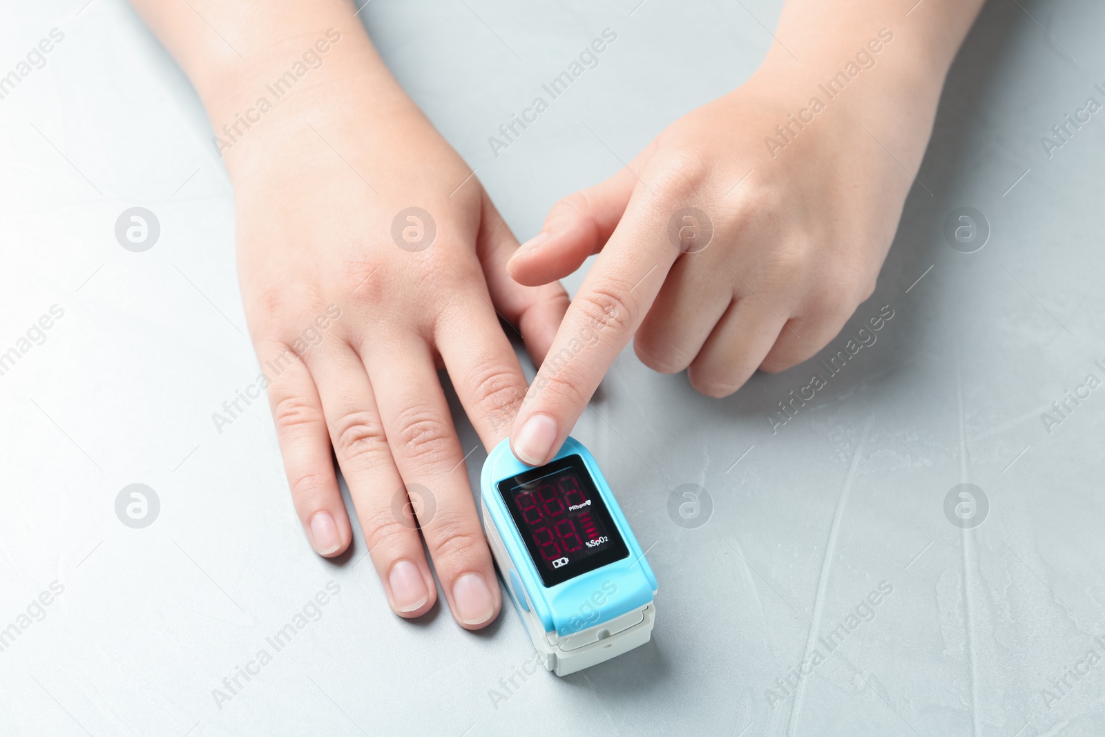 Photo of Woman using fingertip pulse oximeter at light grey stone table, closeup