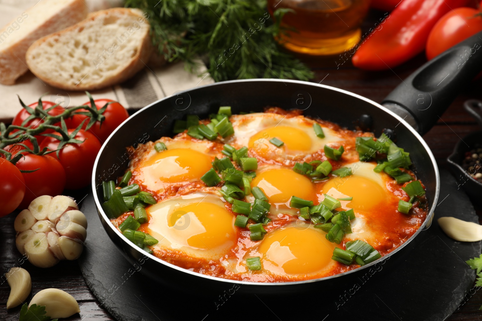 Photo of Delicious shakshuka in frying pan and products on wooden table, closeup
