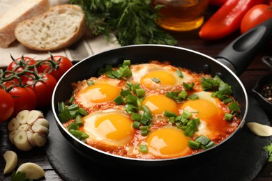Delicious shakshuka in frying pan and products on wooden table, closeup