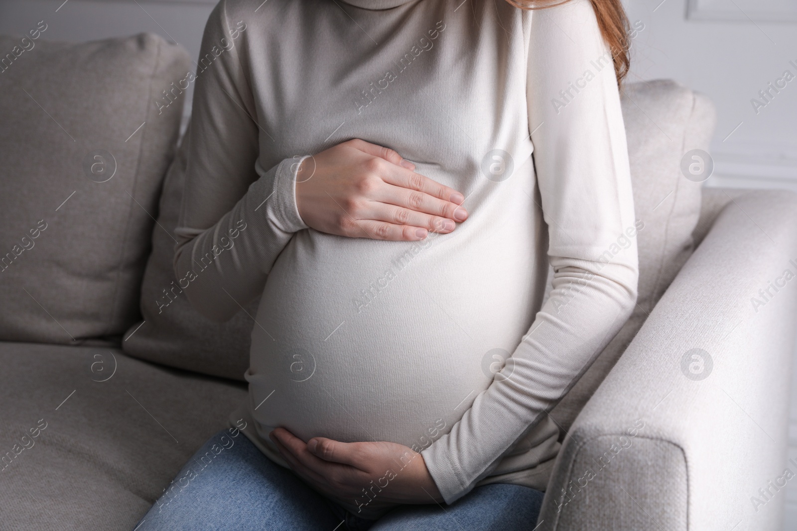 Photo of Young pregnant woman sitting on sofa indoors, closeup