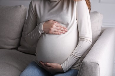 Young pregnant woman sitting on sofa indoors, closeup