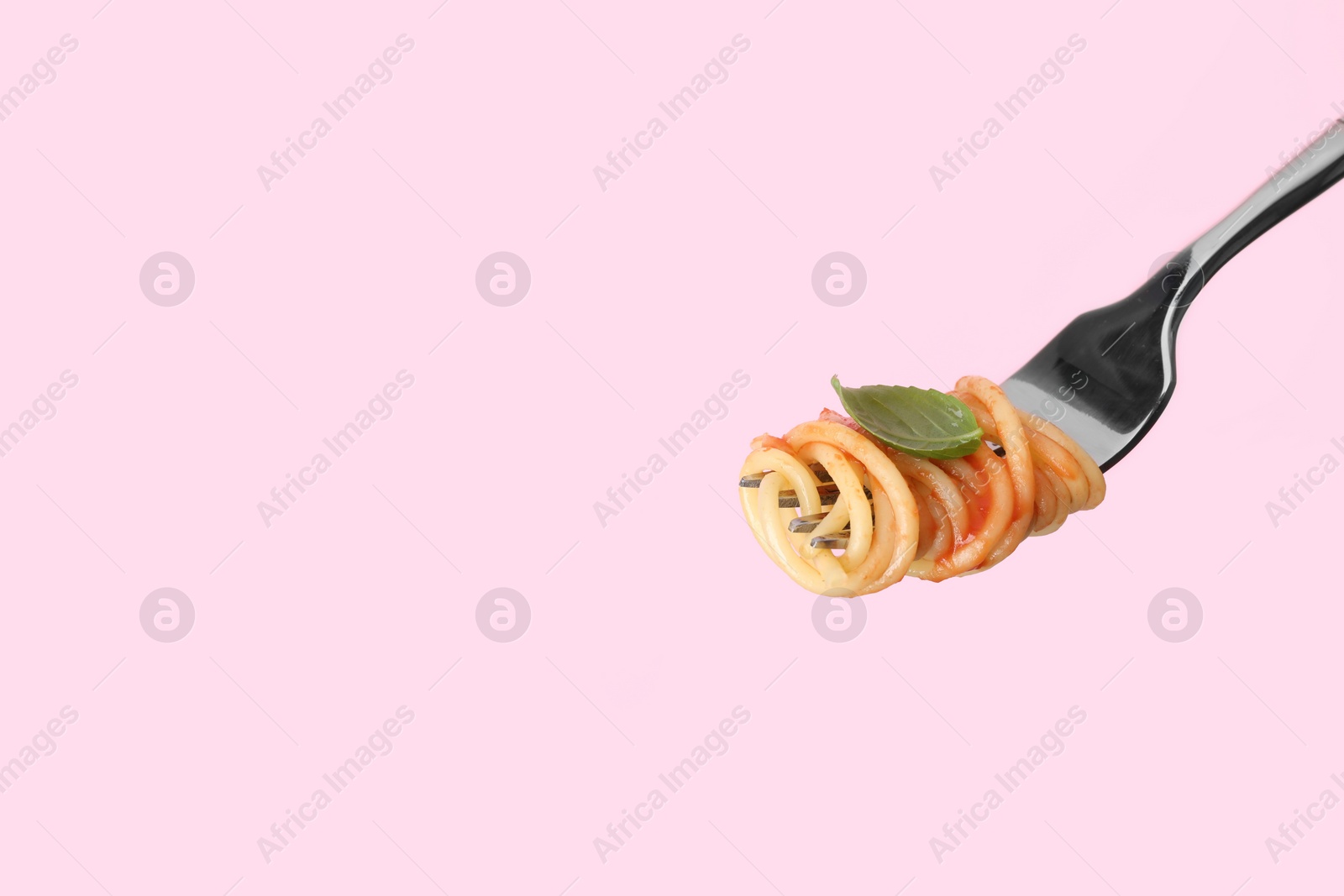 Photo of Fork with tasty pasta, basil and tomato sauce on pink background, space for text