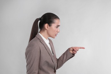 Photo of Emotional woman in suit pointing with index finger on light grey background