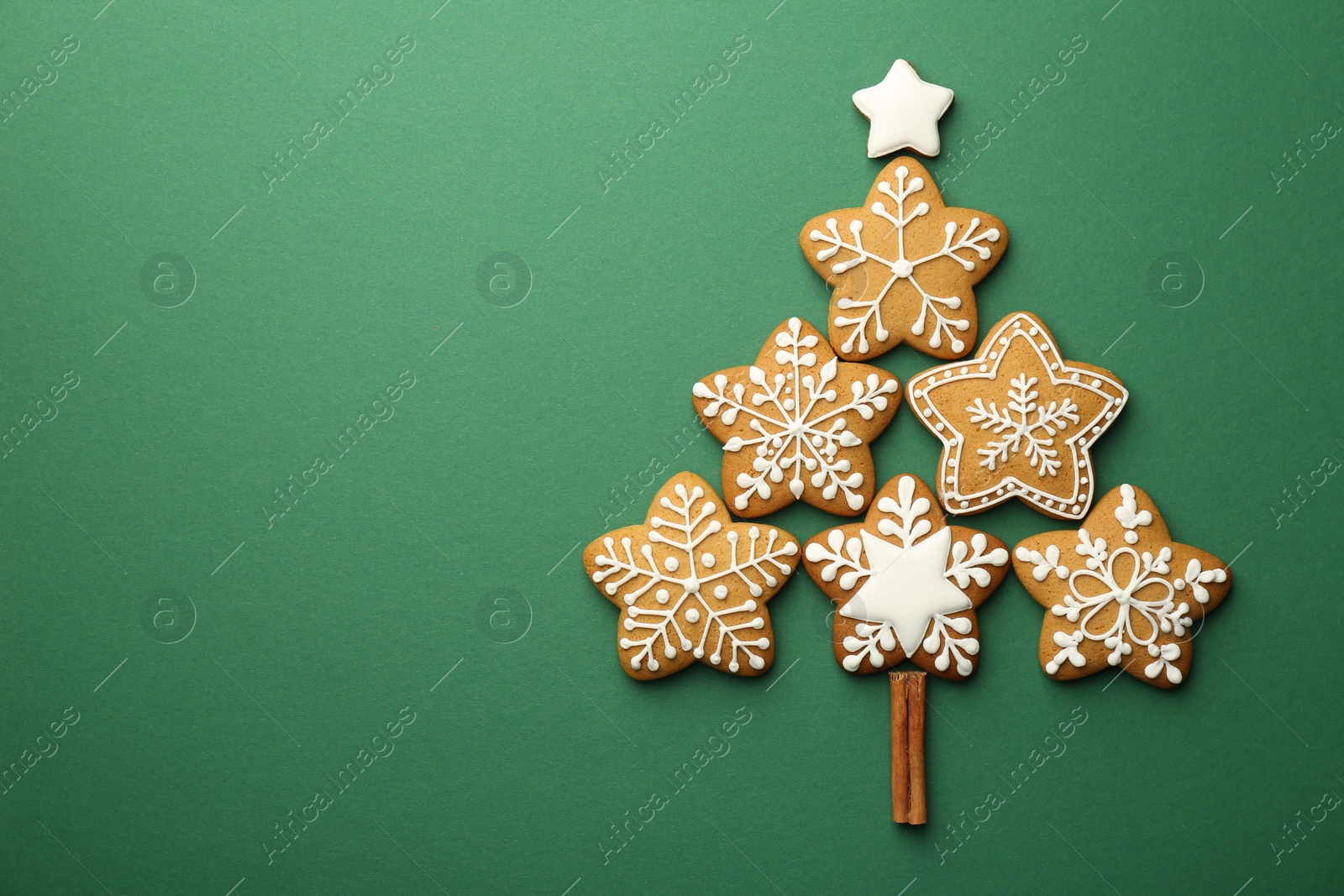 Photo of Christmas tree made of tasty cookies with icing and cinnamon stick on green background, flat lay. Space for text