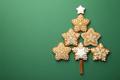 Christmas tree made of tasty cookies with icing and cinnamon stick on green background, flat lay. Space for text