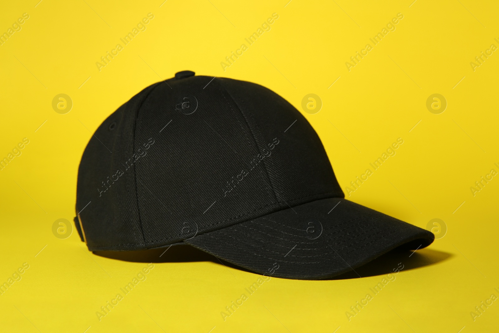 Photo of Stylish black baseball cap on yellow background