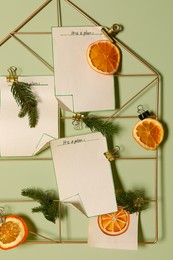 Photo of Christmas decor made of dry orange slices, notes and fir tree branches on light green wall, closeup
