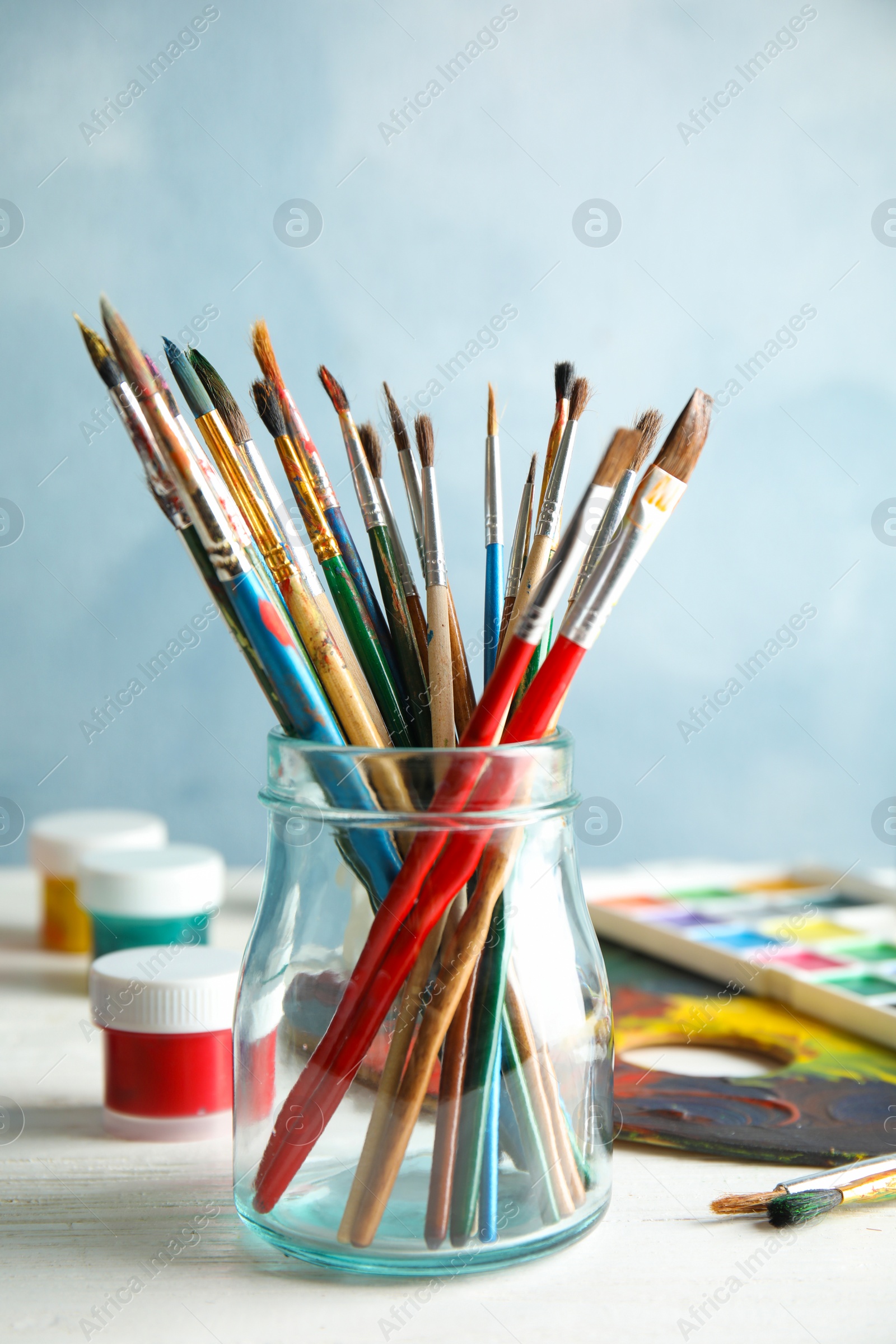 Photo of Glass jar with brushes and paints on table against color background