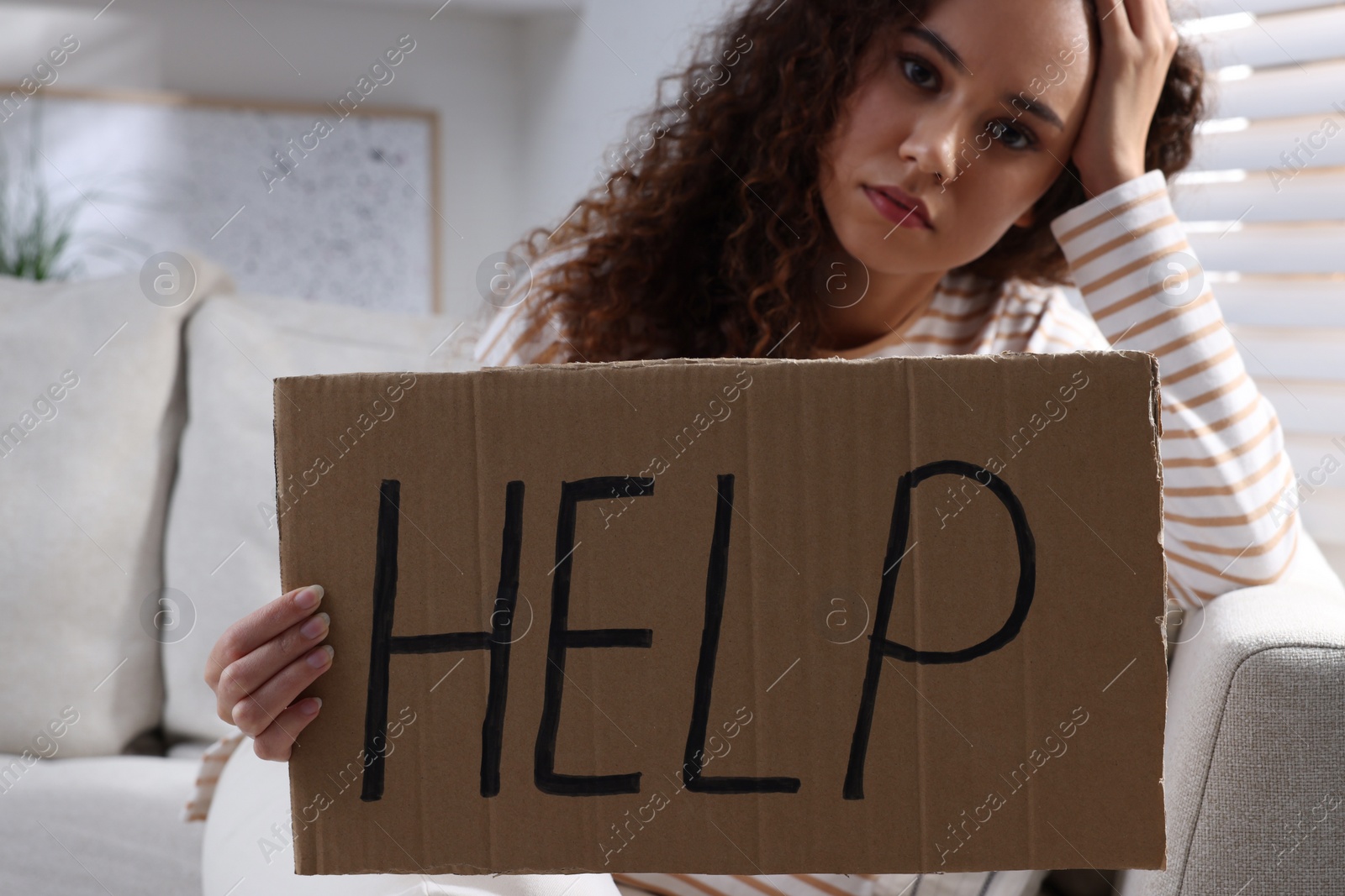 Photo of Unhappy African American woman with HELP sign on sofa indoors