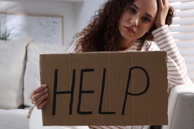 Unhappy African American woman with HELP sign on sofa indoors