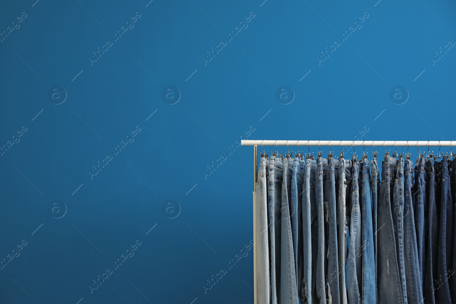 Photo of Rack with stylish jeans on blue background. Space for text