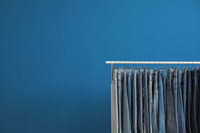 Photo of Rack with stylish jeans on blue background. Space for text