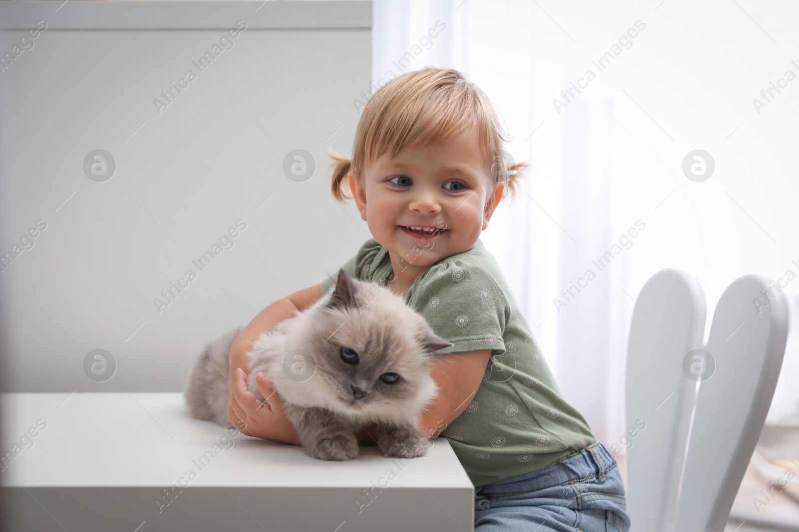 Photo of Cute little child with adorable pet at white table in room