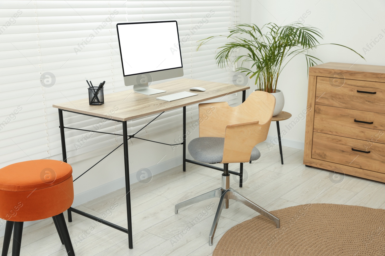 Photo of Stylish office interior with comfortable chair, desk, computer and houseplant