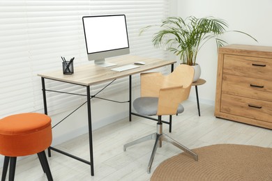 Photo of Stylish office interior with comfortable chair, desk, computer and houseplant