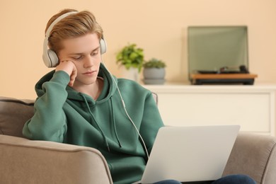 Photo of Teenage boy with headphones using laptop at home