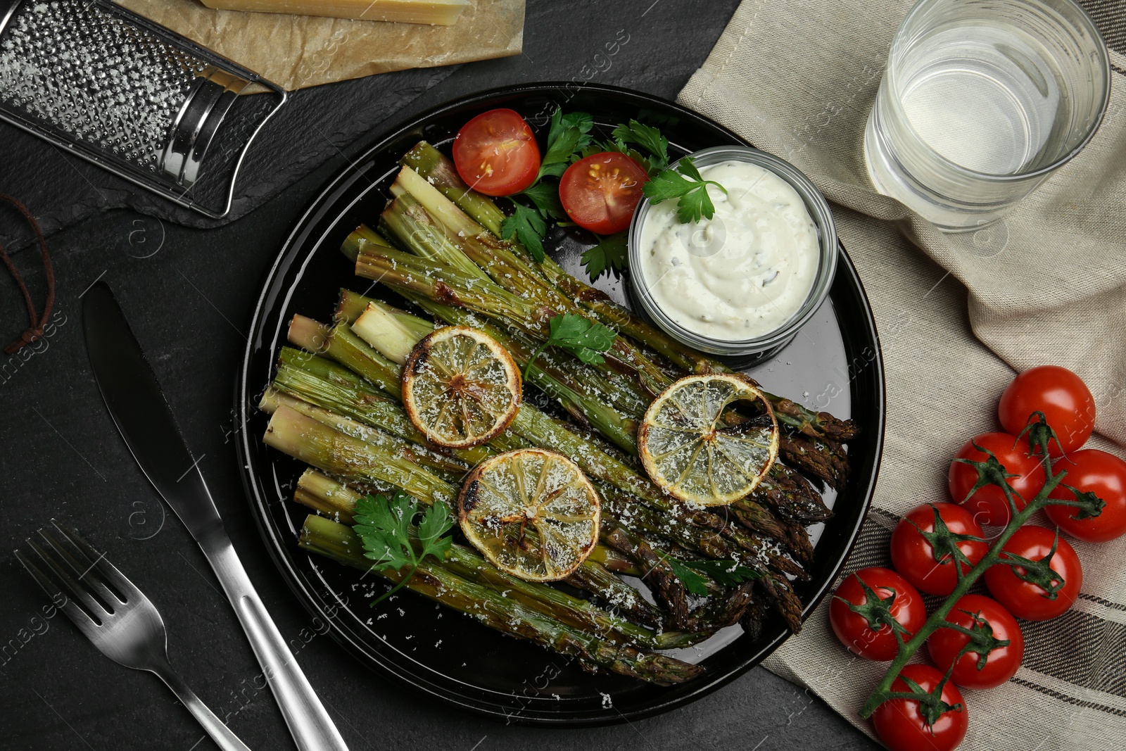 Photo of Oven baked asparagus with lemon slices served on black table, flat lay