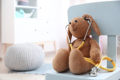 Toy bunny with stethoscope on chair indoors, space for text. Children's doctor