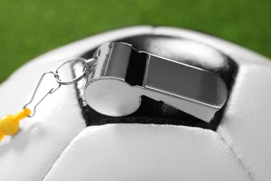 Football referee equipment. Soccer ball and metal whistle on green background, closeup