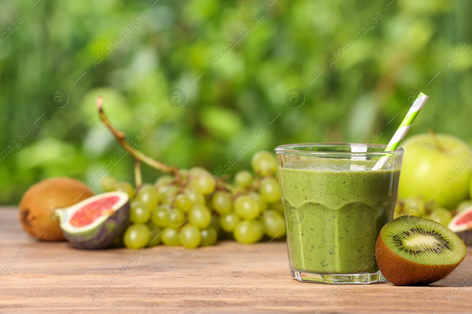 Photo of Glass of fresh green smoothie and ingredients on wooden table outdoors, space for text