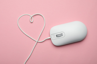 Photo of Computer mouse with heart shaped wire on pink background, top view