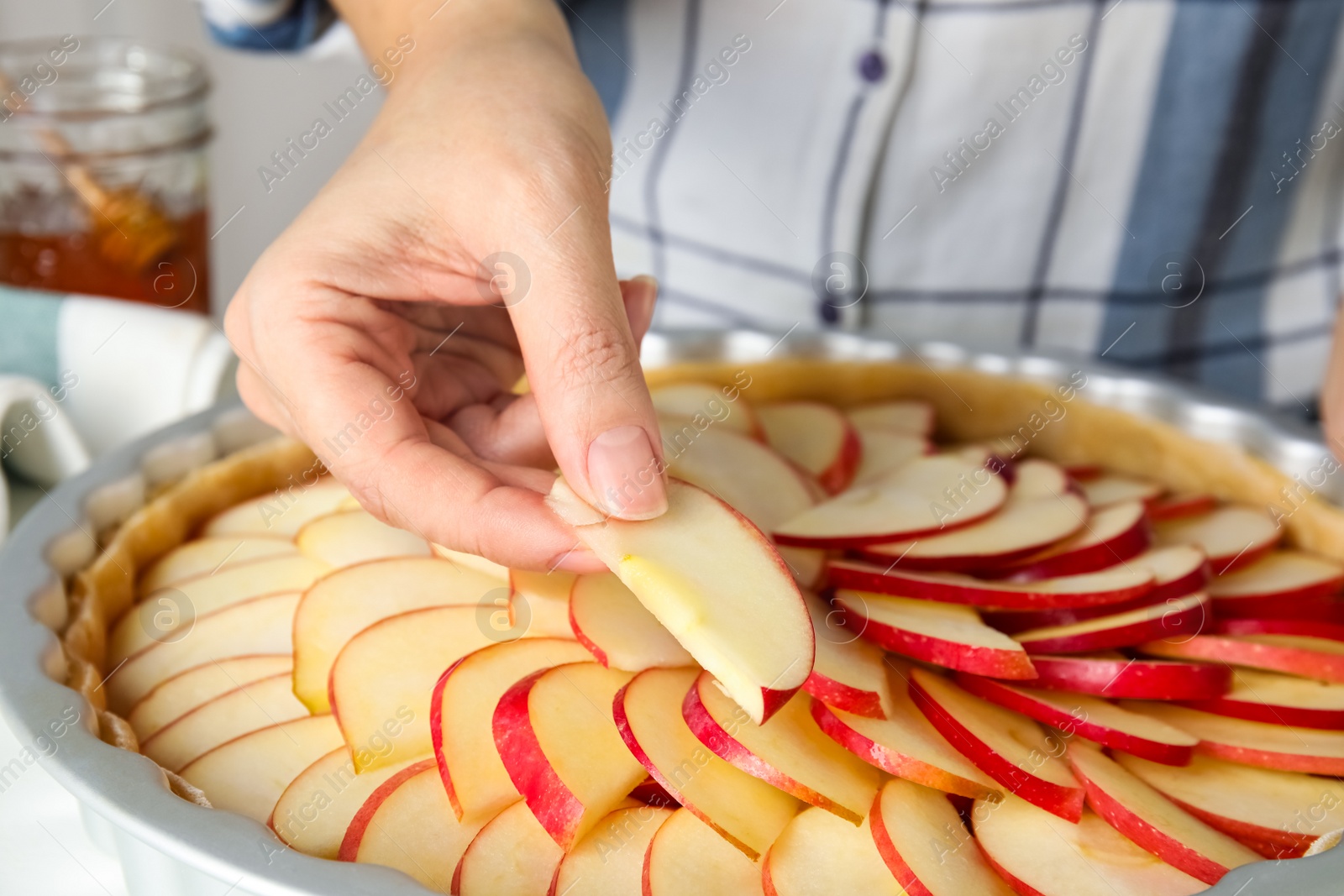 Photo of Woman putting apple slice into baking dish to make traditional English pie, closeup