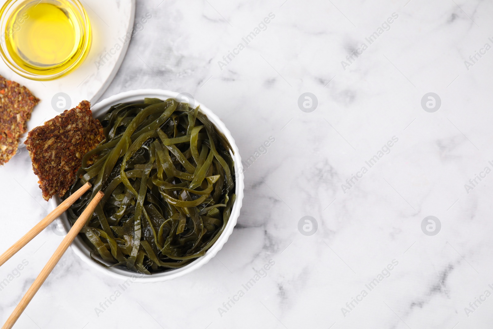 Photo of Tasty seaweed salad in bowl served on white marble table, flat lay. Space for text