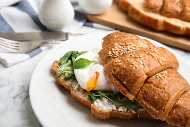 Photo of Delicious croissant with arugula and egg on white marble table, closeup