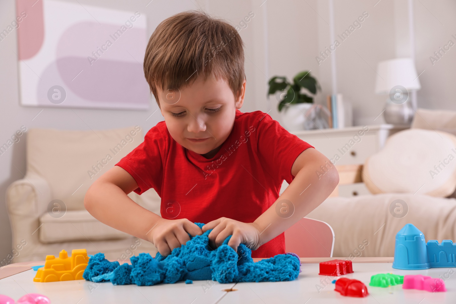 Photo of Cute little boy playing with bright kinetic sand at table in room