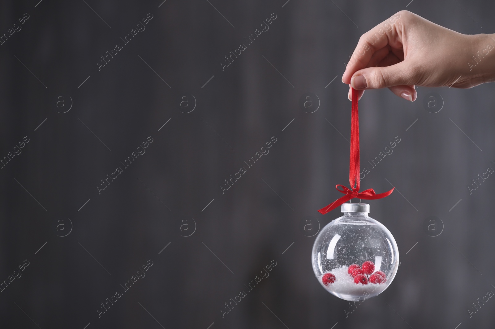 Photo of Woman holding decorative snow globe on grey background, closeup. Space for text