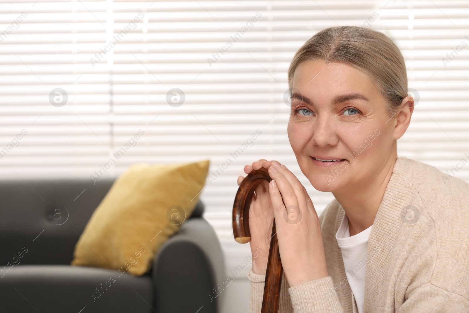 Photo of Senior woman with walking cane sitting on armchair at home. Space for text