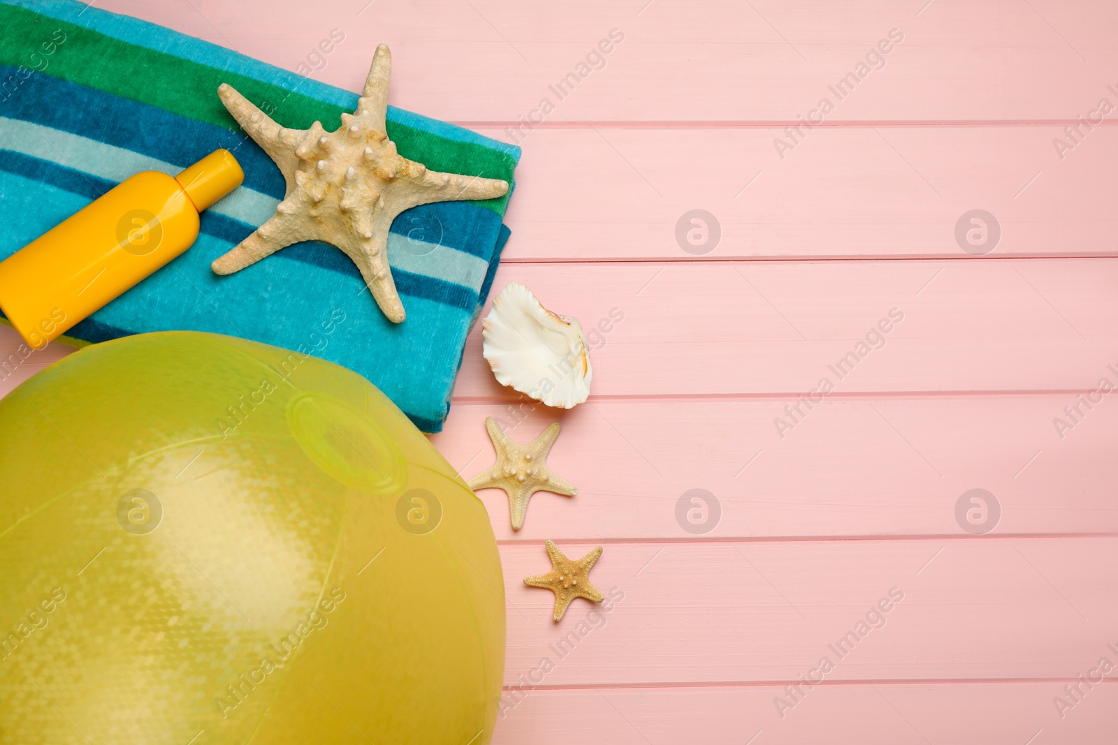 Photo of Beach ball, blanket, sunscreen and starfishes on pink wooden background, flat lay. Space for text