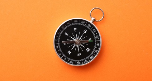 Photo of One compass on orange background, top view