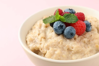 Photo of Tasty oatmeal porridge with raspberries and blueberries in bowl on light background, closeup