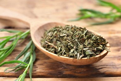 Photo of Spoon of dry tarragon and green leaves on wooden table, closeup