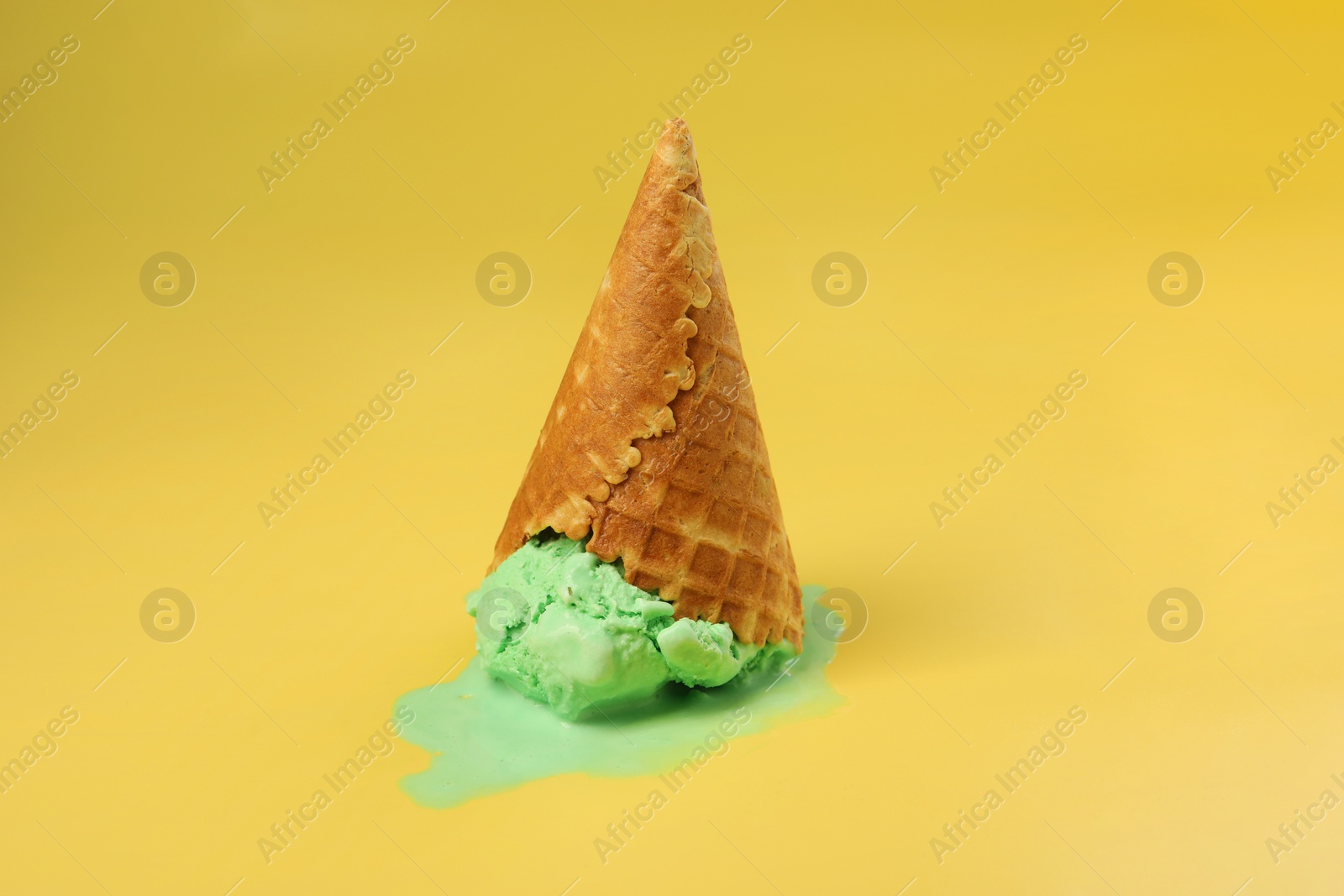 Photo of Melted ice cream in wafer cone on pale yellow background