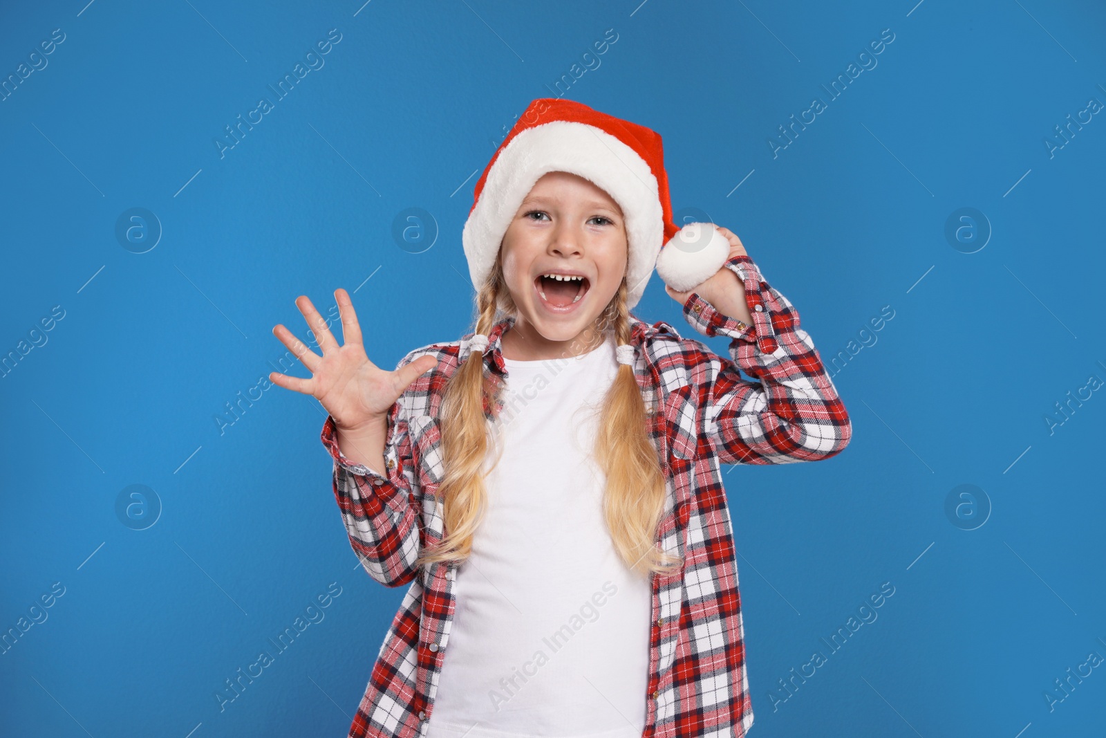 Photo of Excited little child in Santa hat on blue background. Christmas celebration
