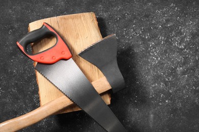 Photo of Saw with colorful handle, axe and log on dark gray textured background, top view. Space for text