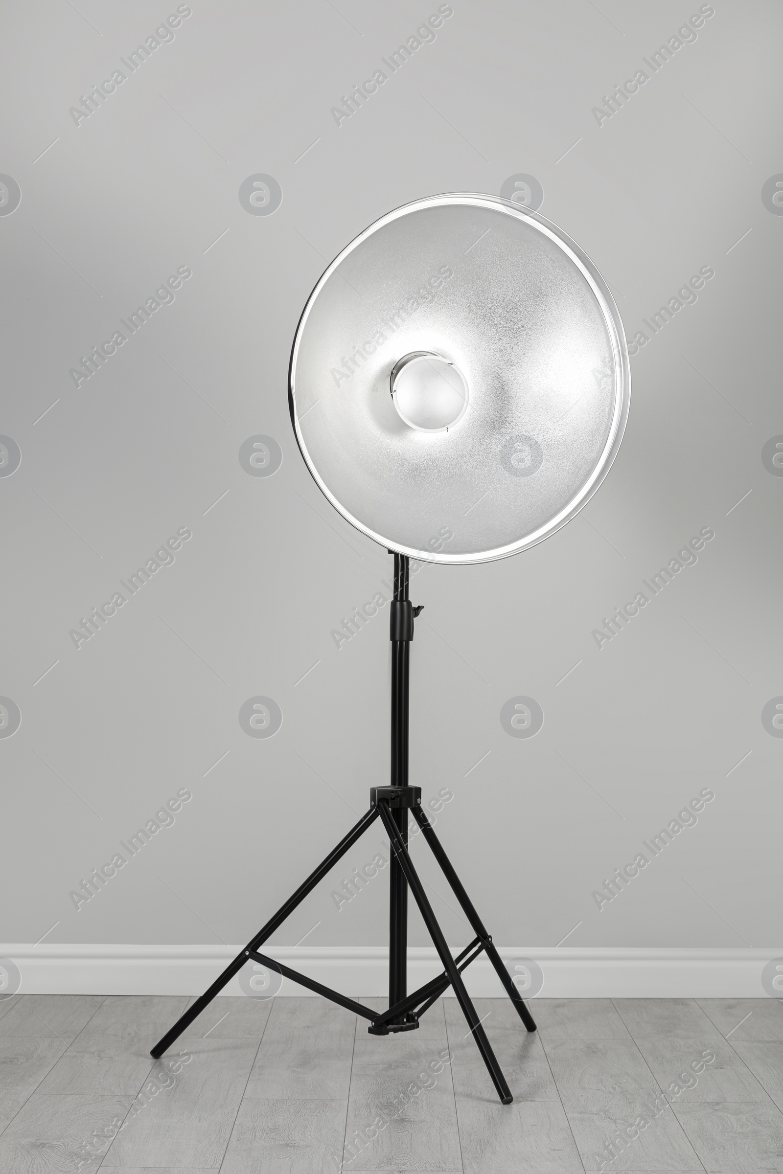 Photo of Professional beauty dish reflector on tripod near grey wall in room. Photography equipment