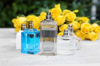 Photo of Perfumes and beautiful bouquet of yellow roses on light table outdoors, selective focus