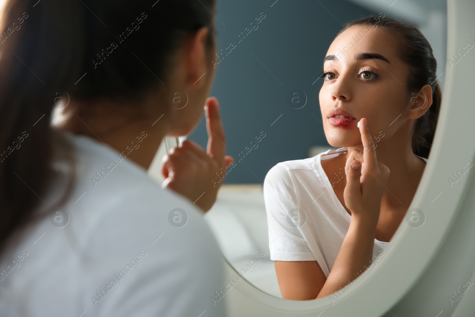 Photo of Young woman with herpes applying cream on lips in front of mirror at home