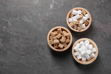 Different sugar cubes in bowls on gray textured table, flat lay. Space for text