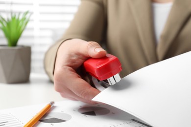 Woman with papers using stapler at white table indoors, closeup