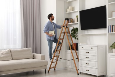 Man with books on wooden folding ladder at home